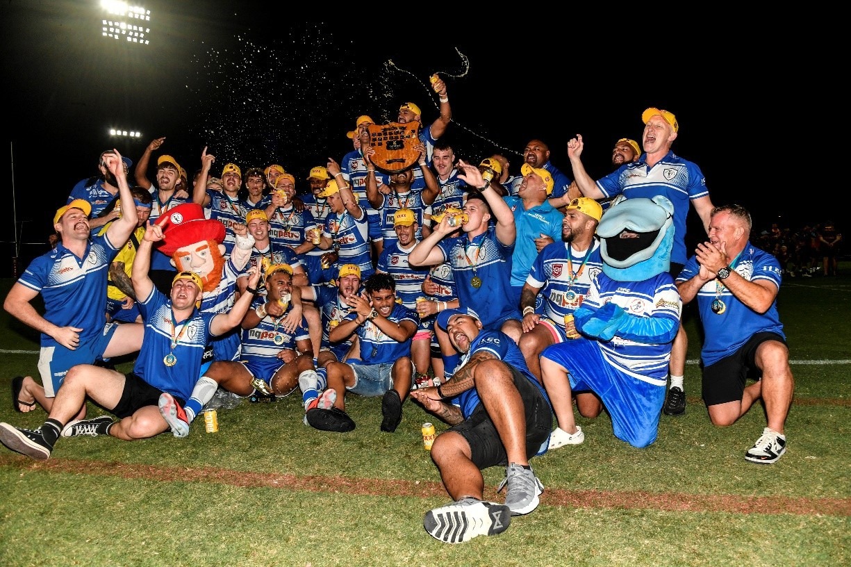 Mens ruby team celebrating win, captain holding winners plaque. Night time with water flying in air.