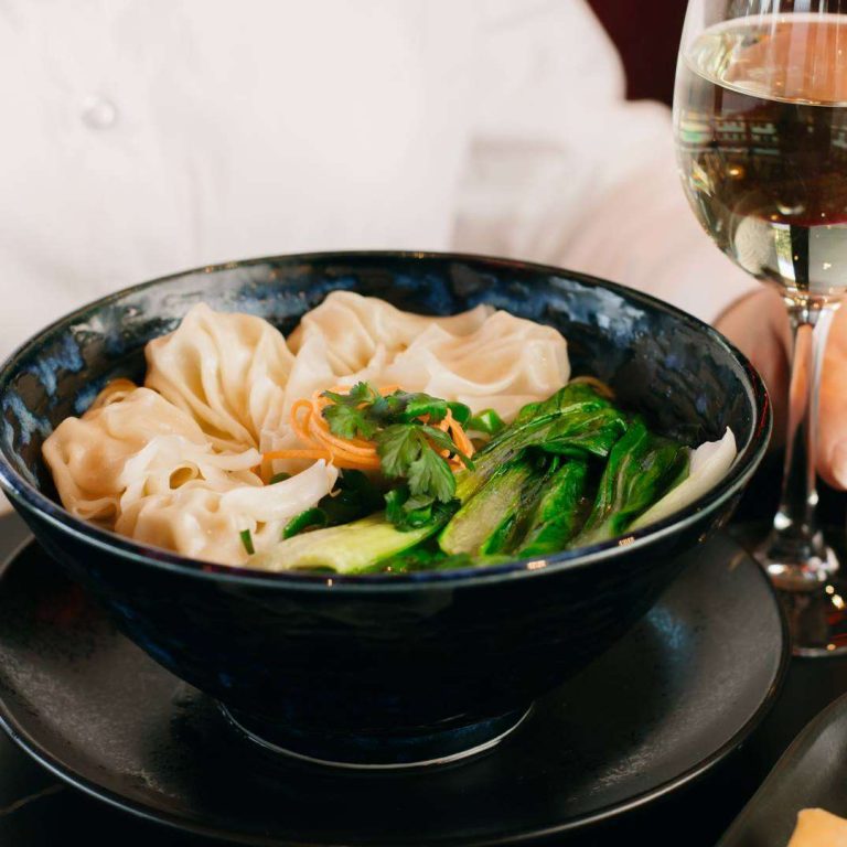 Steamed dumplings with bok choy and fresh herbs served in a bowl beside a glass of white wine at Wok O’Clock Cairns.
