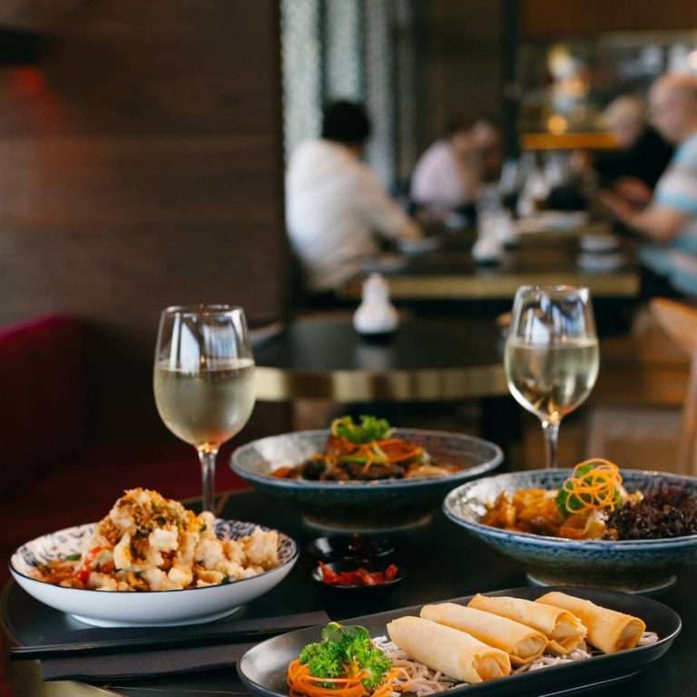 Asian-inspired dishes, including spring rolls and shared bowls, served with glasses of white wine at Wok O’Clock Cairns.